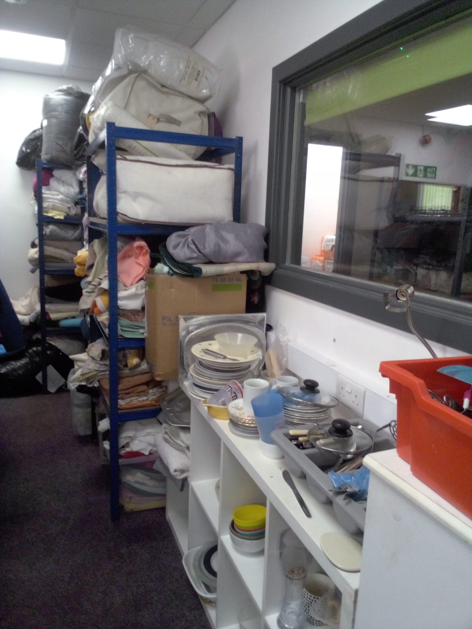 Shelves of folded bedding and bags, beside shelves of plates, bowls and saucepans.