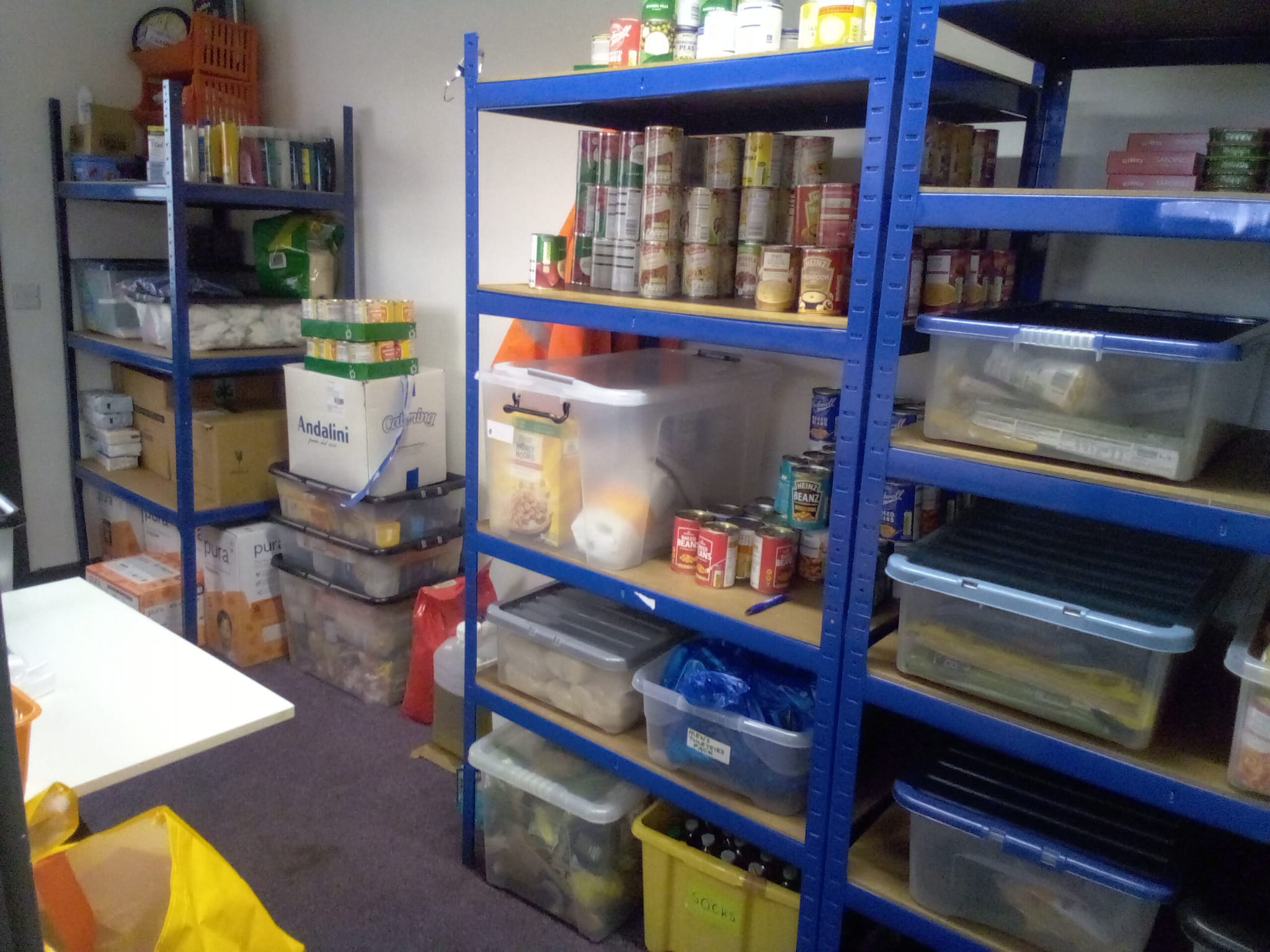 Shelves stocked with tinned food and storage boxes of dry food in the food area.